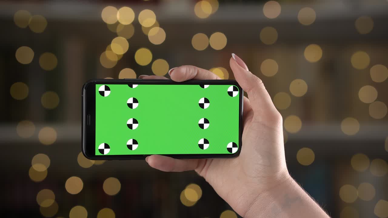 Mobile in horizontal orientation with alpha compositing on display is in woman hand against bokeh