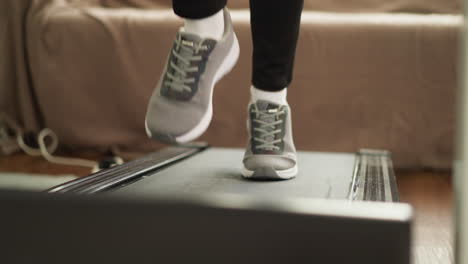 lady runs on treadmill at home closeup. athletic woman keeps wellness by engaging in legs workouts on automatic device in personal fitness center