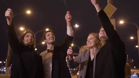 group of friends wearing elegant clothes holding sparklers and hugging in the street after the new year's party