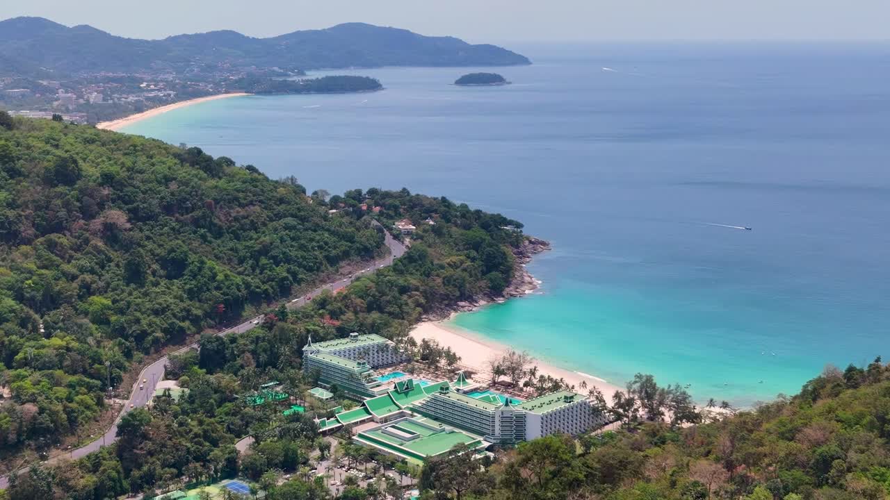 Drone footage captures Phuket's lush greenery and turquoise waters, showcasing a luxury resort nestled along the coastline under bright daylight