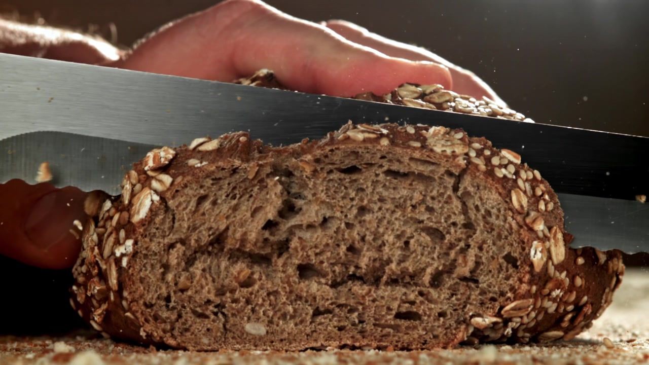 Nahaufnahme einer Hand, die in Zeitlupe frisches Vollkornbrot schneidet