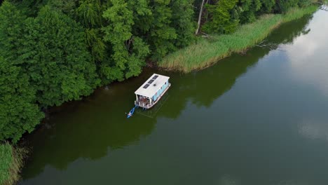 Small-house-boat-floating-on-a-lake-surrounded-by-a-forest-in-Brandenburg,-Germany