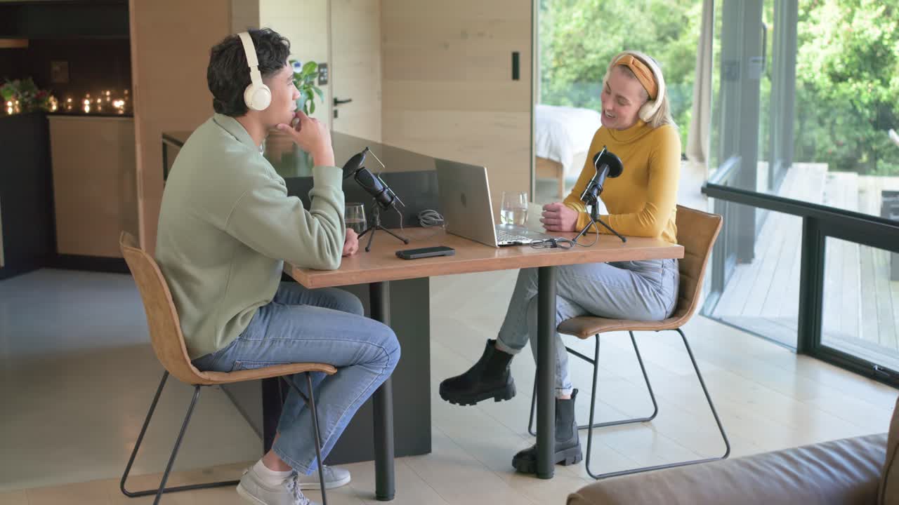 Mężczyzna podnosi rękę, a różni współpracownicy omawiają podcast w studiu, korzystając z mikrofonów i laptopa