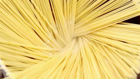 Raw-spaghetti-arranged-in-silver-pot-filled-with-water-ready-to-be-cooked-on-wooden-table