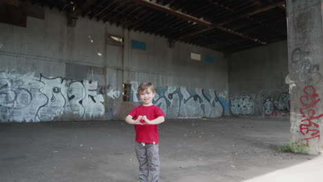 a young little boy is having fun and making heart symbols with hands in front of camera in a red t-shirt, camera zooming up