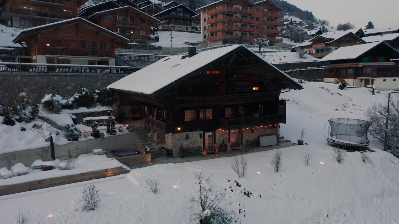 drone volando lentamente hacia una lujosa casa de vacaciones en una pequeña ciudad suiza en invierno