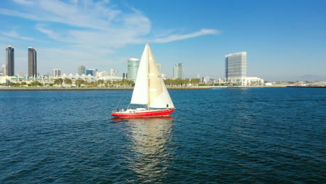 red sailboat on the san diego bay with a view of san diego's skyline