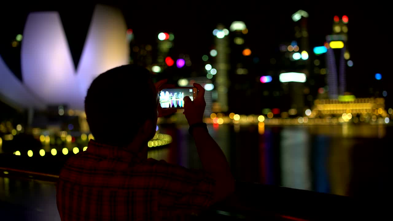 男性がスマートフォンで夜の街の写真を撮っている。