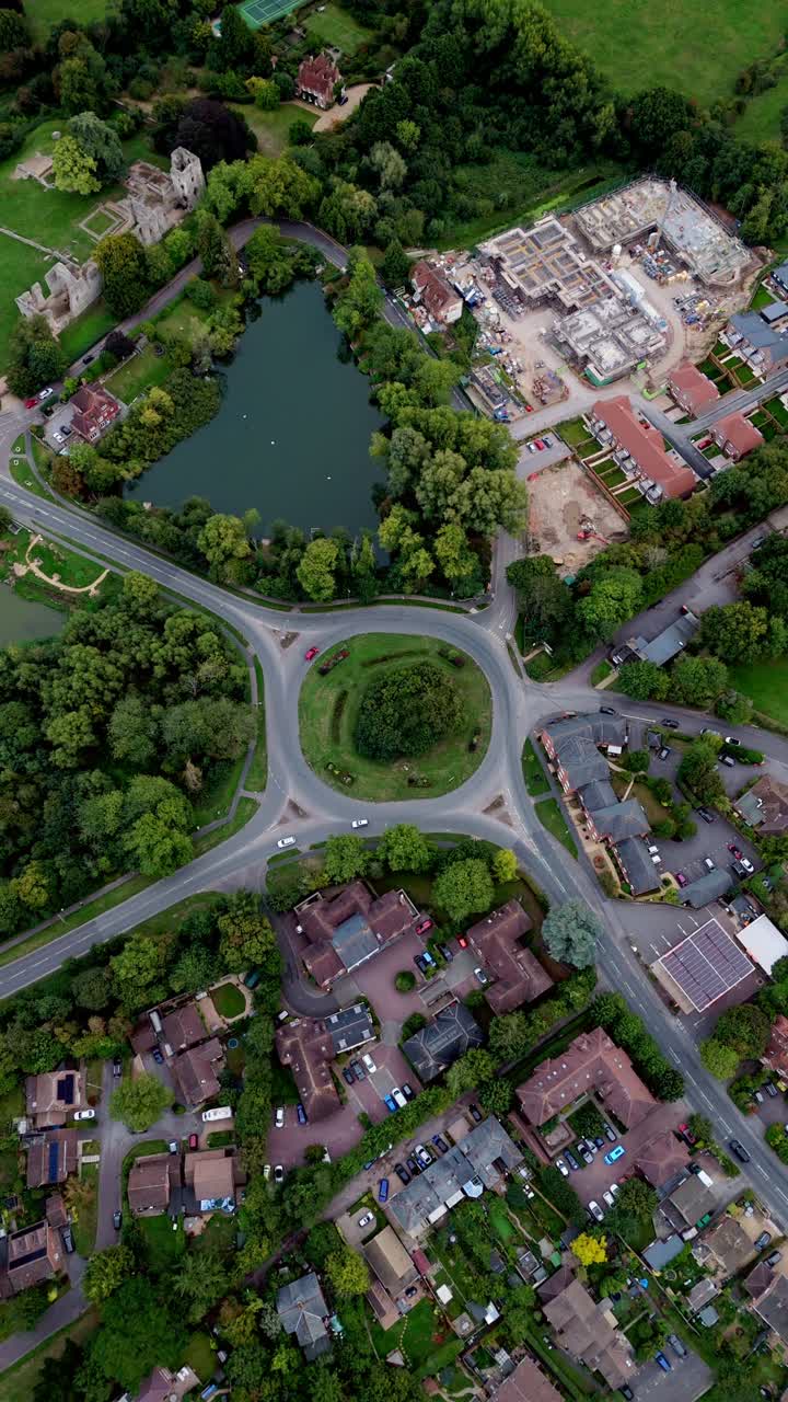 High wide-angle portrait aerial drone view of Bishop’s Waltham roundabout with pond, surrounded by autumn trees, village streets, and glowing warm sunset light across the scenic town landscape