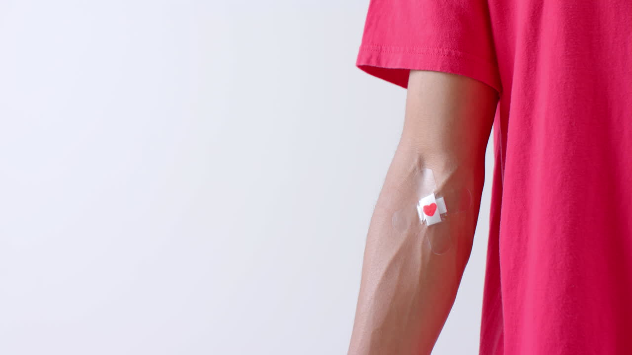 sección media de un hombre biracial con el corazón pegando yeso en el brazo, en blanco con espacio de copia, cámara lenta