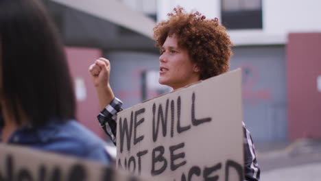 Diverse-group-of-men-and-women-holding-placards-shouting-raising-fists-during-protest