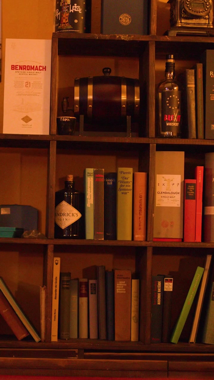 Warmly lit bar interior, wooden shelves lined with books and whiskey bottles, slow camera pan