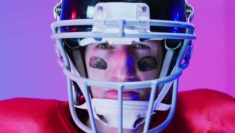 Video-of-portrait-of-caucasian-american-football-player-in-helmet-over-neon-purple-background