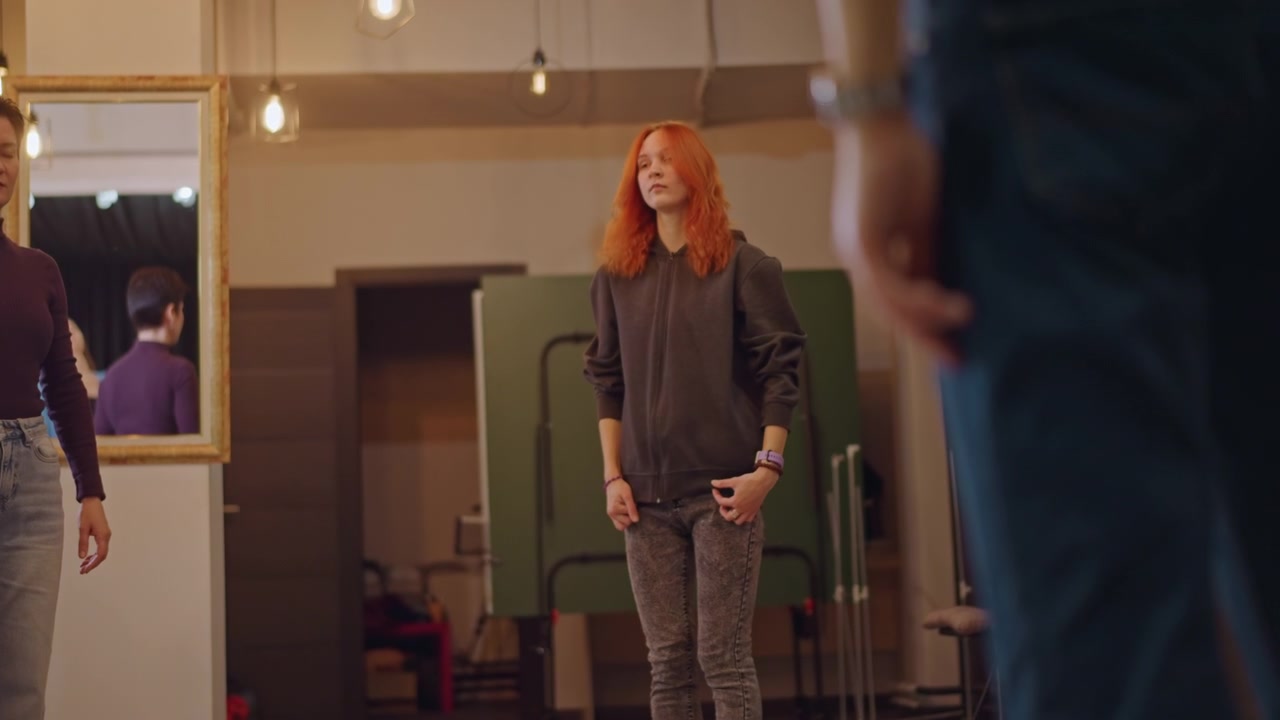 Two students stretching in rehearsal studio, vocal coach guiding warmup before performance, mirror reflection, soft lighting, breathing and posture exercises, casual clothing, cooperative atmosphere