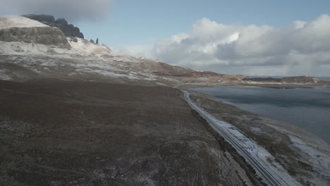 The-skye-bridge-area-in-scotland,-showcasing-a-serene-landscape-with-a-train-traveling-along-the-coast,-winter-season,-aerial-view