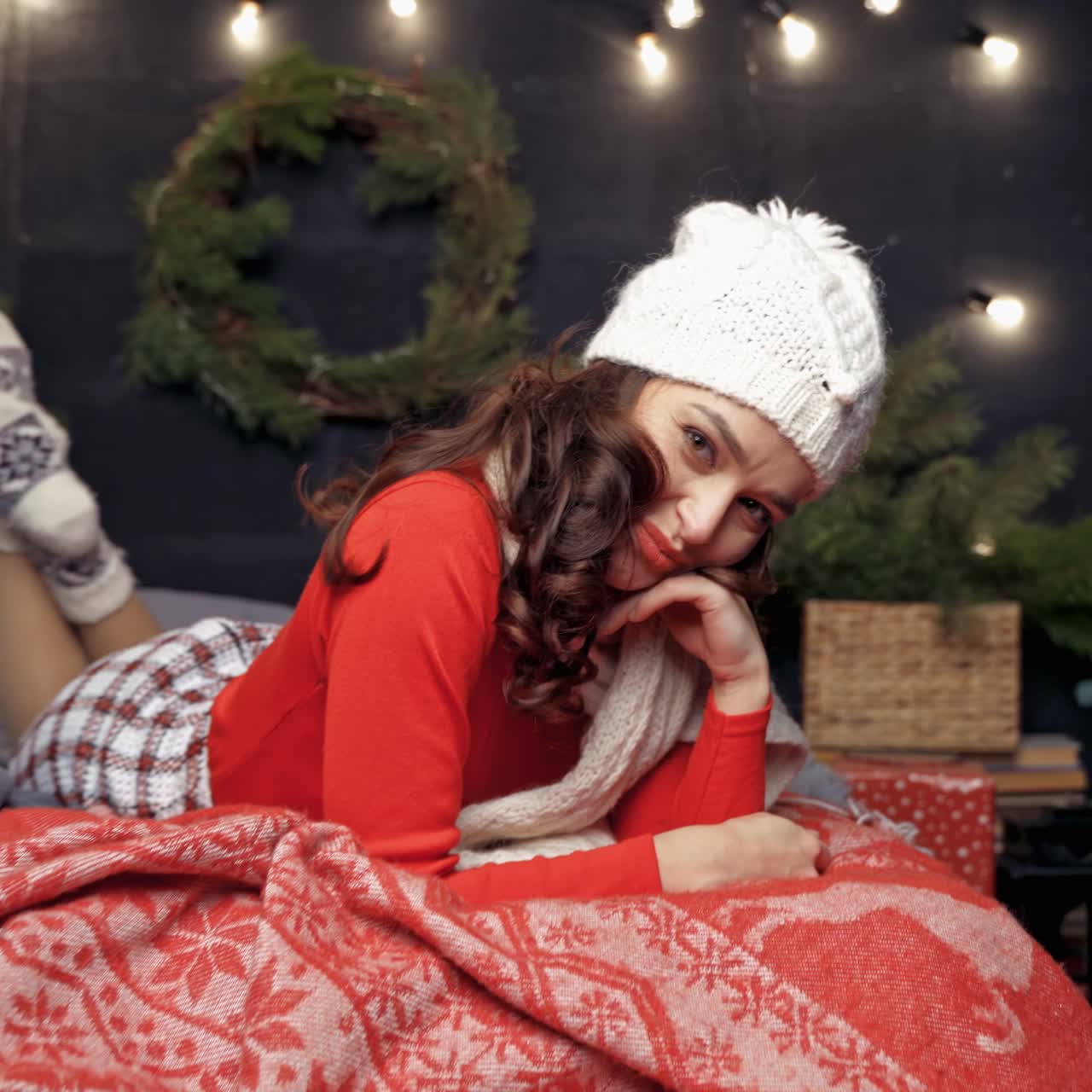 Woman in red sweater Santa and white hat laying on bed posing to the camera. Happy New Year merry holiday concept video