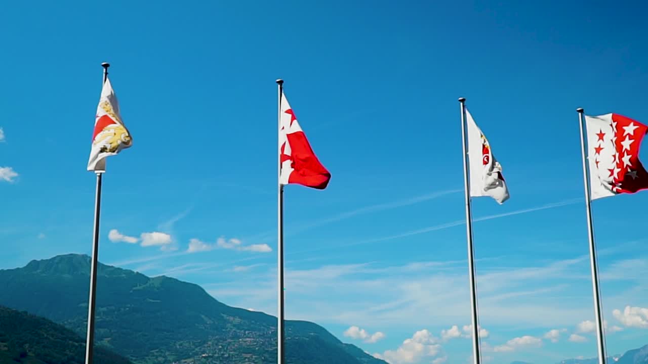 Four Swiss flags fly against blue sky blowing in wind slow motion