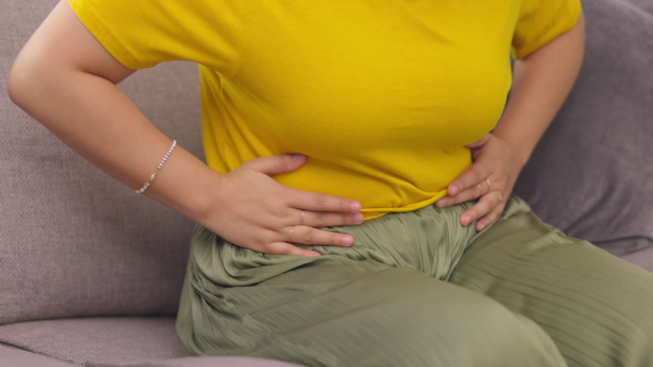 Stomach pain, hands and woman on a sofa with pms