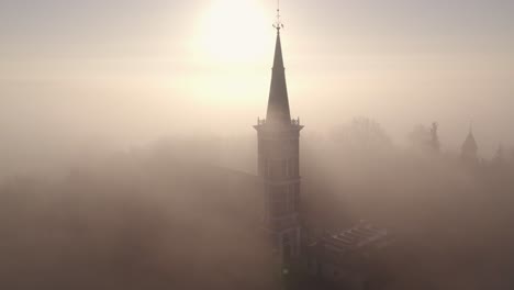 Traditional-dutch-church-at-Friesland-with-dense-morning-fog,-aerial