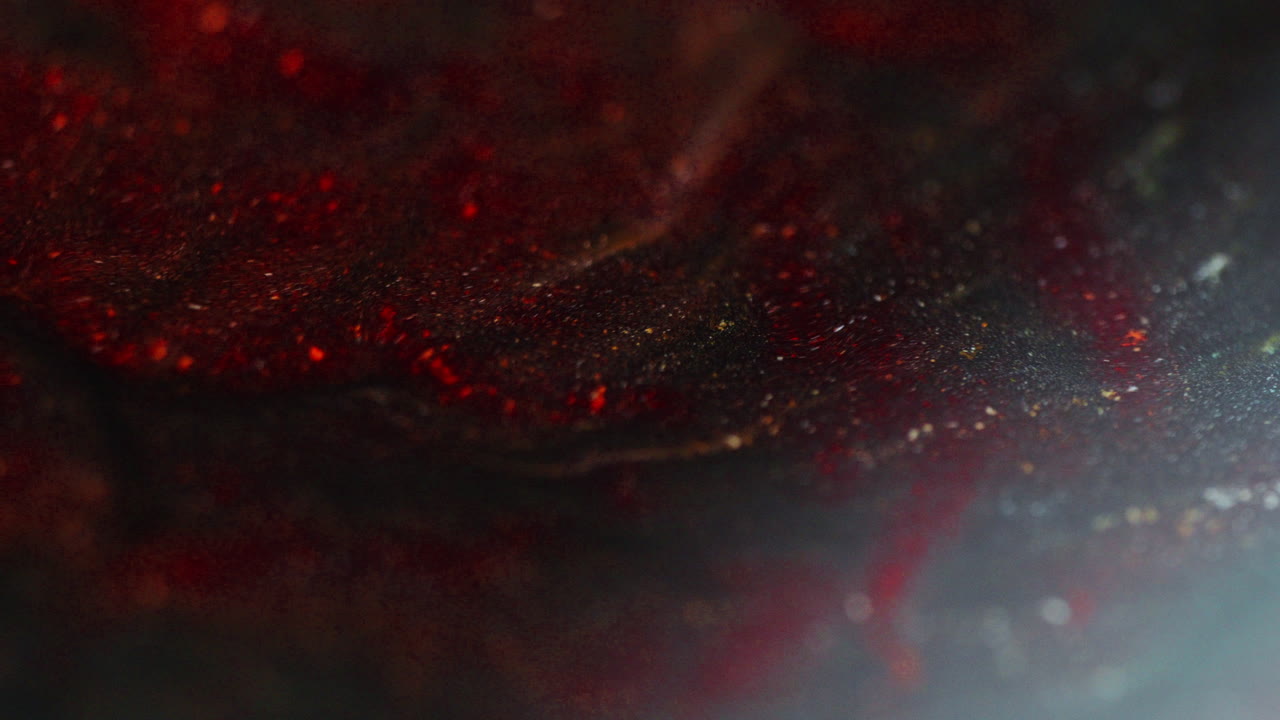 Macro shot of burgundy ink with orange reflections being drawn to the left side of the frame, creating glowing abstract patterns