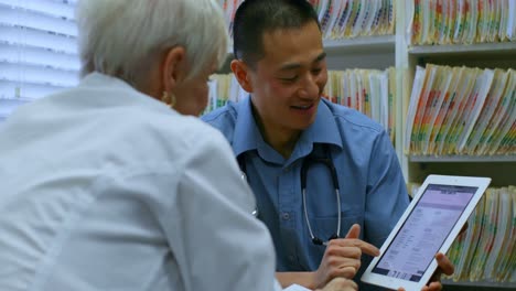 Young-Asian-male-doctor-and-senior-patient-discussing-over-digital-tablet-in-the-clinic-4k