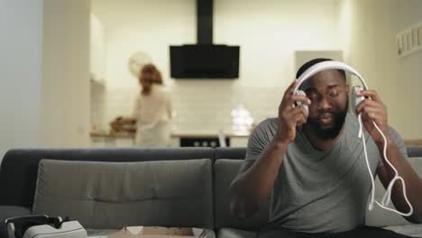 black man putting headphones at open kitchen. smiling guy making dance movement