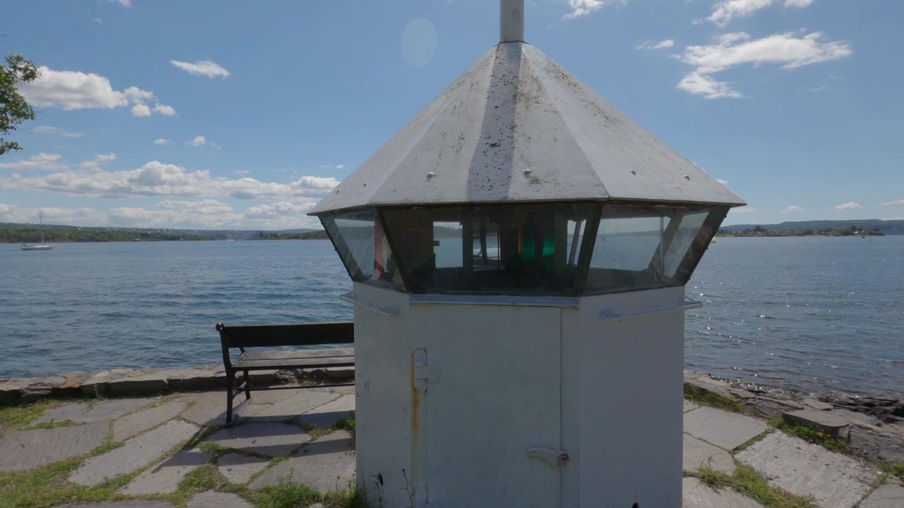 Maritimes Navigationsleuchtfeuer an einer gepflasterten Uferpromenade neben ruhigem Fjordwasser.