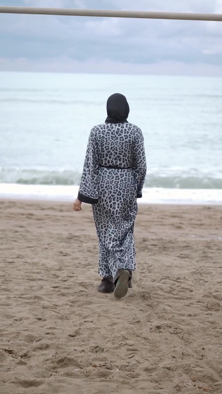 Woman in Hijab and Leopard Print Dress Walking on Beach