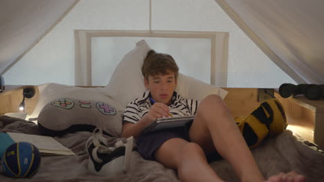 teenage boy relaxing in bed and writing in a notebook