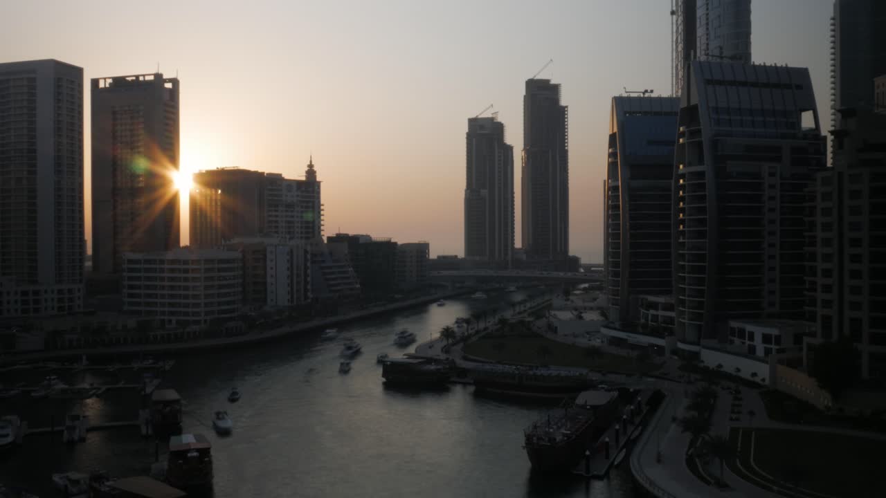 A beautiful timelapse of the sunset at Dubai Marina (an affluent residential district of the United Arab Emirates): the sun falling between two skyscrapers, boats navigating the water channel.