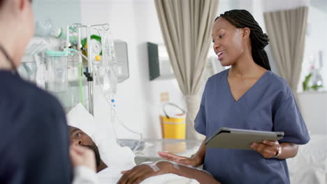 diverse female doctors and male patient talking in hospital room, slow motion