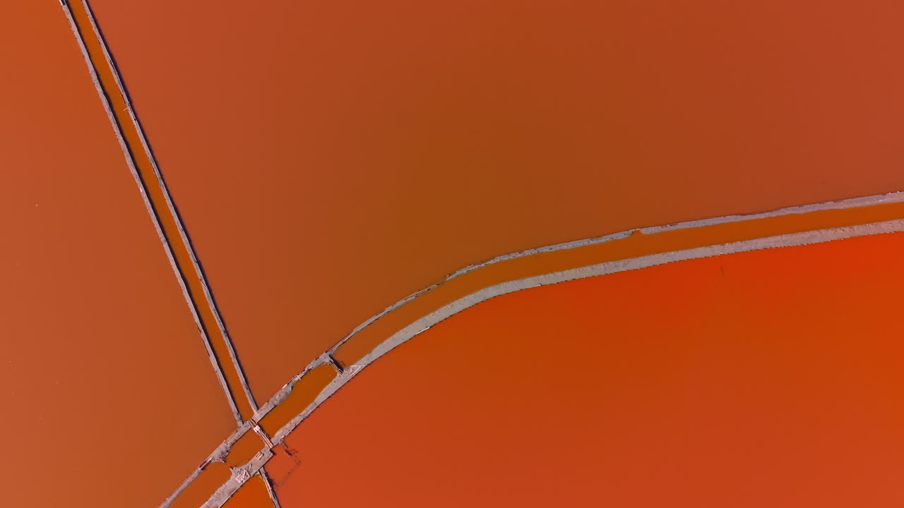 Minimalistisk vy uppifrån av orange saltdammar för avdunstning. Abstrakt flygbild av orange mineraldammar delade av smala stigar och industriella strukturer.