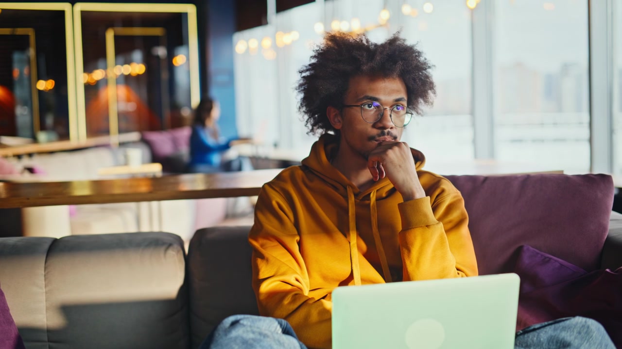 African american freelancer pondering ideas laptop. Remote worker relaxing sofa.