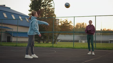 volleyball beginner being observed by instructor while serving with performance book and whistle in hand, coach taking notes and tracking progress on outdoor court during training