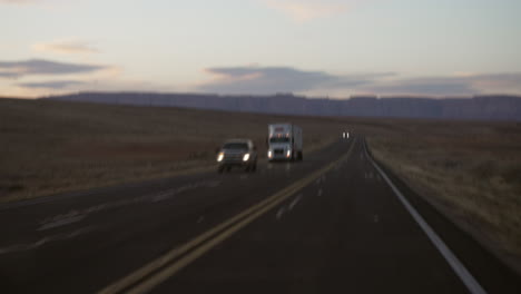 Bumpy-desert-road-passing-cars-on-roadtrips-and-a-freight-truck-at-dusk