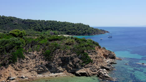 aerial: reveal drone shot of tsougkria island beach where tourist boats and sailboats are moored while tourists swim in turquoise clear blue water