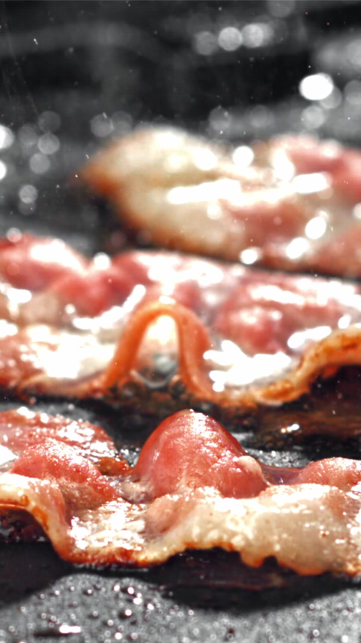 Deliziose striscioline di pancetta che sfrigolano e friggono in una padella calda