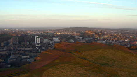vista aérea ascendente desde los riscos de salisbury en el parque de holyrood para revelar la ciudad de edimburgo al amanecer, escocia