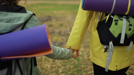 Unrecognizable-couple-backpackers-walking-by-forest,-holding-hands-together-close-up