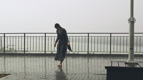 funny woman in dress stands holding heeled shoes in puddle