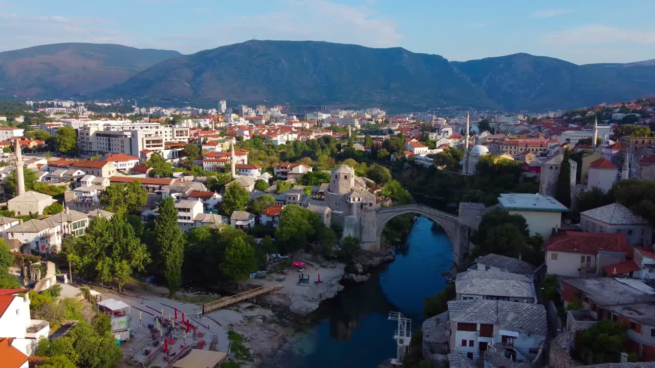 Quiet summer's morning in Mostar with view of iconic Ottoman Mostar Bridge and mountains in background - Bosnia and Herzegovina