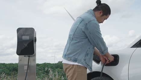 progressive man with his ev car and wind turbine as concept of renewable energy.