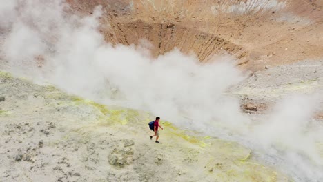 man excursionist walking trough volcano sulfuric smokes, tilt down camera toward crater