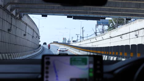 a car navigates a phuket underpass using gps. bright daylight illuminates the urban landscape, highlighting the road's curvature and surrounding structures