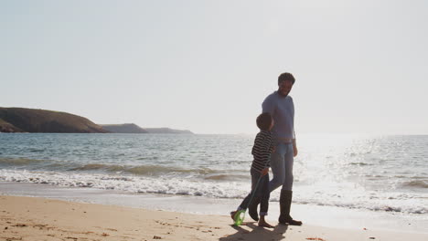 father and son walking along beach by breaking waves on beach with fishing net