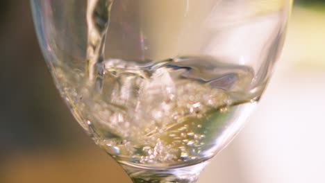 fresh chilled french white wine being poured into glass in ultra slow motion with swaying splashing motion and bubbles rising. luxury alcoholic summer beverage with shallow depth of field.