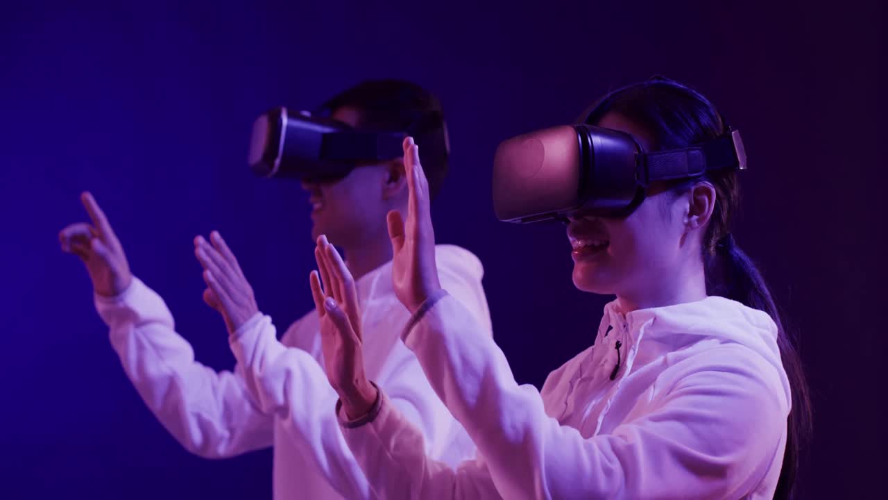 Asian man and woman using vr headsets, touching virtual screen on blue background, slow motion