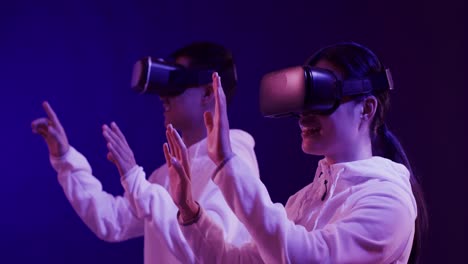 asian man and woman using vr headsets, touching virtual screen on blue background, slow motion