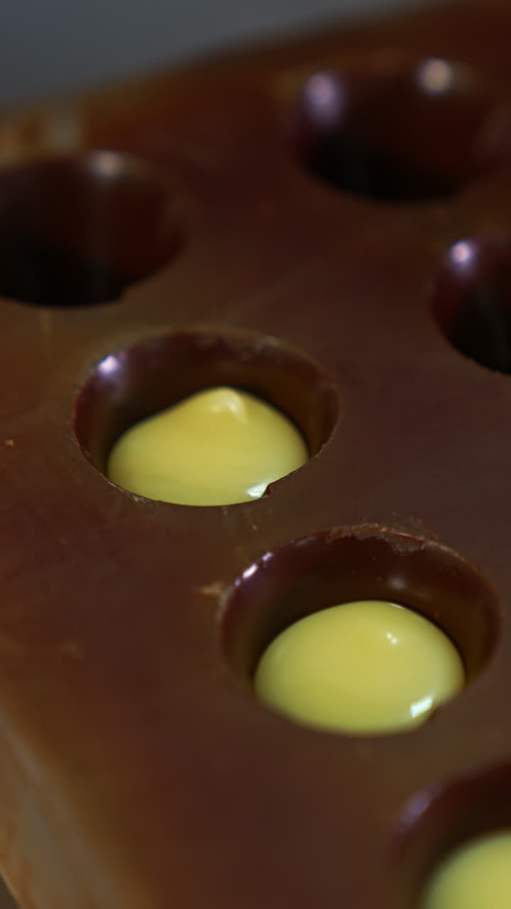 Molds already covered with chocolate are filled with white stuffing. Gloved hand squeezes the filling into the molds from pastry bag. Close up. Vertical video