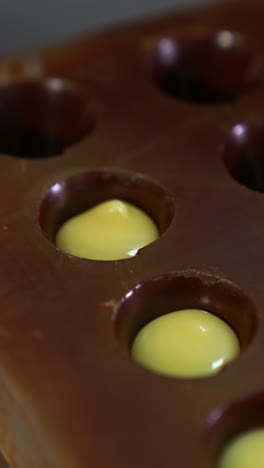 molds already covered with chocolate are filled with white stuffing. gloved hand squeezes the filling into the molds from pastry bag. close up. vertical video